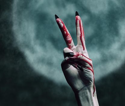 Vampire hand in blood on background of full moon, peace hand sign. Halloween or horror theme