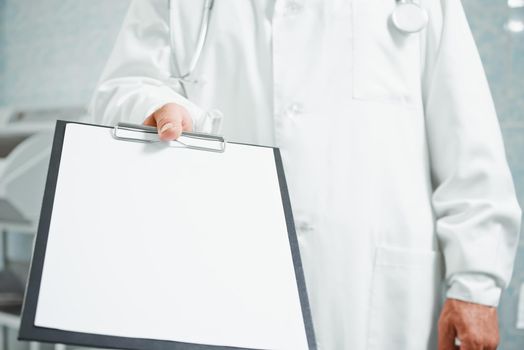 Unrecognizable older doctor holds out empty clipboard, space for text