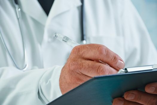 Unrecognizable older man doctor writes medical records on clipboard