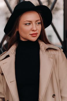 Stylish young woman in a beige coat in a black hat on a city street. Women's street fashion. Autumn clothing.Urban style.