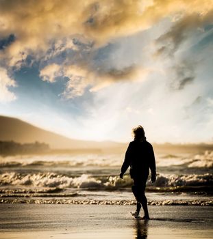 Silhouette of the man, walking on the ocean beach at sunset