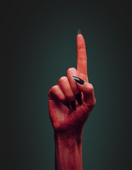 Red devil hand with gesture pointing upward on dark background, space for text. Halloween or horror theme
