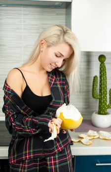 the Woman in the kitchen in home clothes cleaning fruit pomelo with emotions