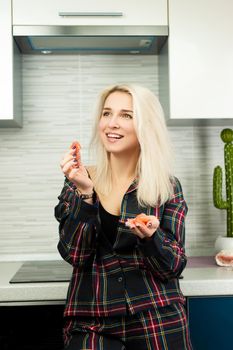 the woman in the kitchen in home clothes with a peeled pomelo fruit eats and laughs