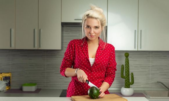 the blonde vegan woman cuts avocado in kitchen