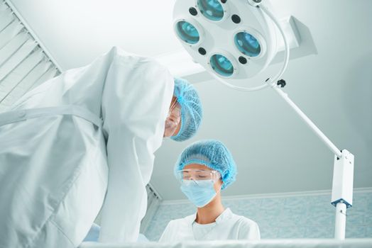 Two surgeons are working in operating room on background of surgical lamp, teamwork