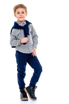 Cute boy standing against white background. Little boy wearing gray shirt, jeans and boots. Portrait of cheerful kid posing with blue pullover tied around the neck