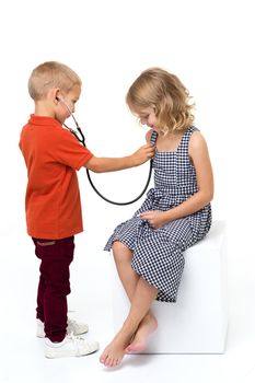 Cute children playing doctor and patient. Younger brother using stethoscope to listen his sister heart. Adorable children having fun at home isolated on white background