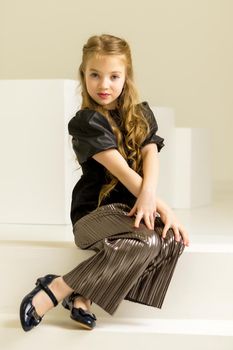 Beautiful little girl poses for a magazine in the studio on a white cube.