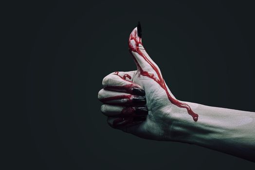 Vampire hand in blood with thumb up gestureon dark background. Halloween or horror theme