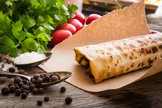 burrito on parchment with vegetables and spices on a wooden background