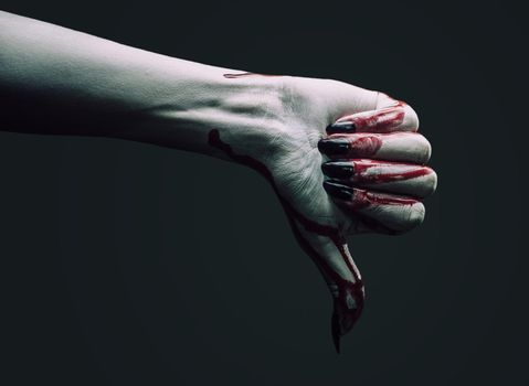 Vampire hand in blood with thumb down gesture on dark background. Halloween or horror theme