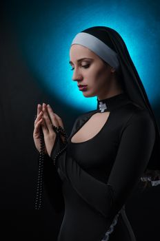 The Fine art portrait of a novice nun in deep prayer with rosary