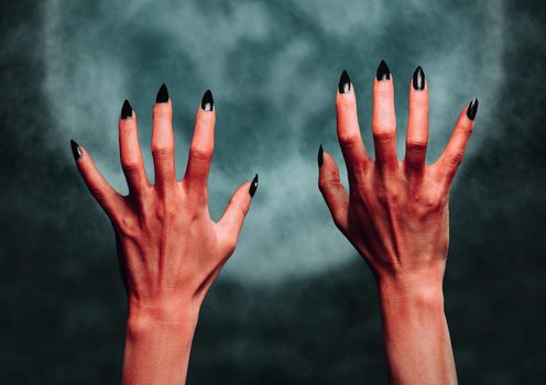 Red hands of the devil on background of full moon. Halloween or horror theme