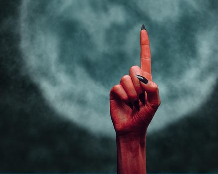 Red devil hand with gesture pointing upward on background of full moon, space for text. Halloween or horror theme