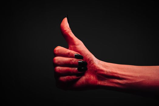 Red demon or devil hand with thumb up gesture on dark background. Halloween or horror theme