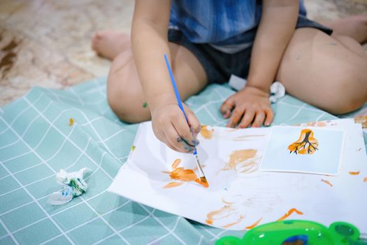 Focus on hands on paper. Children use paintbrushes to paint watercolors on paper to create their imagination and enhance their learning skills