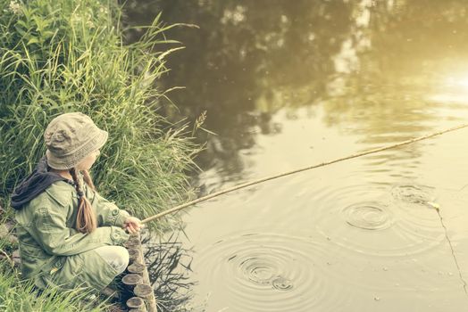 little fisher girl sitting on a river bank with a rod