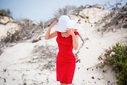 beautiful young woman in evening red dress and white hat on a background of a sand desert