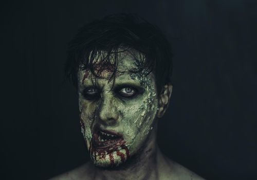 Portrait of scary zombie man on dark background, Halloween makeup