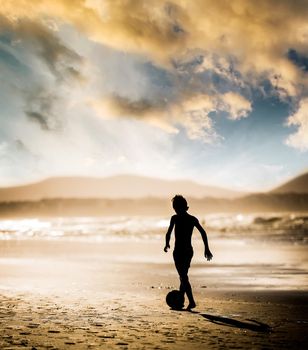 Silhouette of boy on the beach, playing football at sunset
