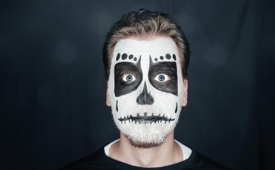 Portrait of surprised young man with skull makeup. Halloween face art