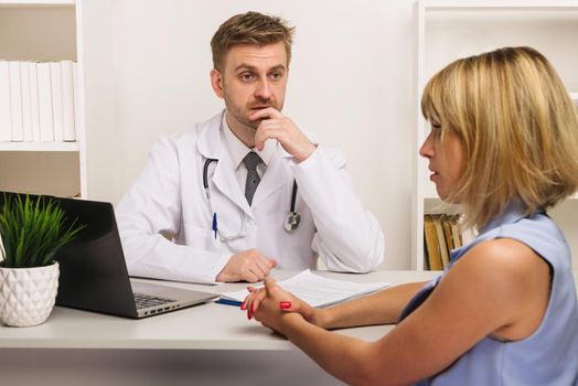 Young woman on a consultation with a male surgeon or therapist in his office. Selective focus on the doctor.