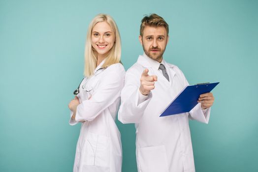 Happy medical team of doctors, man pointing to camera and smiling woman, isolated over blue background