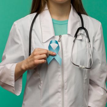 Blue ribbon for prostate cancer awareness campaign and men's health care concept with symbolic bow in doctor's hand - image