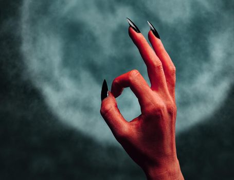 Red demon or devil hand with gesture OK on background of full moon. Halloween/horror theme