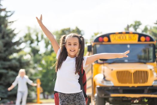 Kids student running into mother's hands to hug her after back to school near the school bus