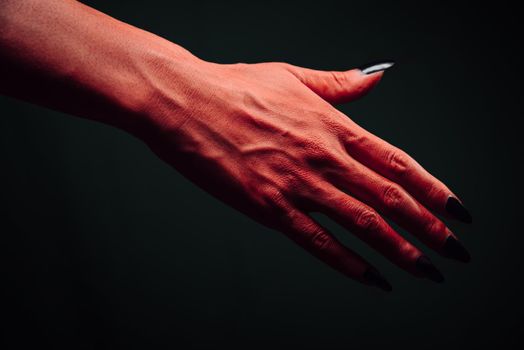 Red demon or devil hand with handshake gesture on dark background. Halloween or horror theme