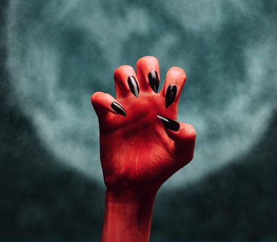 Scary red devil hand on background of full moon. Halloween or horror theme