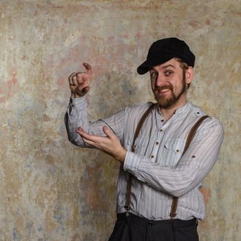 Portrait of handsome young man in white shirt and bow tie adjusting his suspenders and smiling at camera while standing isolated near old wall