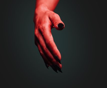 Red demon hand with handshake gesture on dark background. Halloween or horror theme