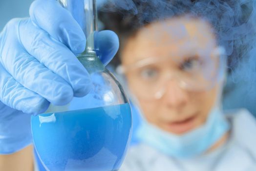 Crazy scientist examines flask with blue liquid, focus on flask