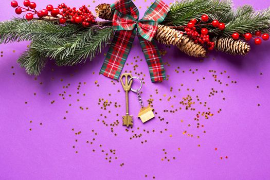 House key with keychain cottage on a festive background with Christmas tree, lights of garlands. Happy New Year-purple background, gift, greeting card. Purchase, construction, relocation, mortgage