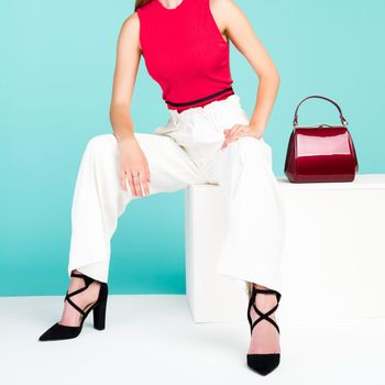 Beautiful woman sitting on the bench with red handbag purse and high heel shoes. - image