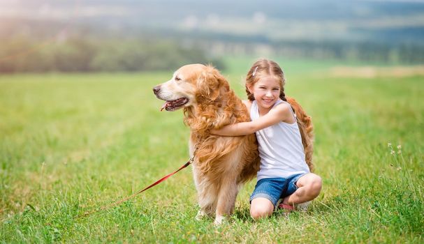 Little girl hugging retriever in the summer park