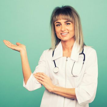 Smiling young female doctor with a stethoscope shows something on the palm on a blue background