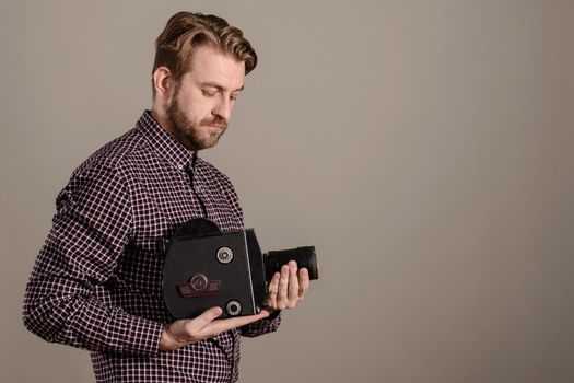 Cameraman in a checkered shirt gently holds an old movie camera in his hands isolated on gray background