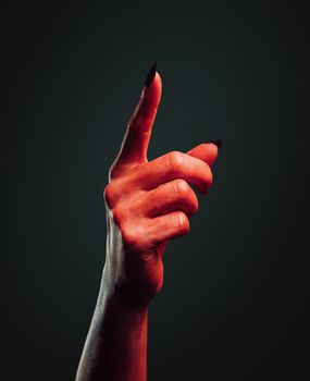 Red demon hand with gesture pointing upward on dark background, space for text. Halloween or horror theme