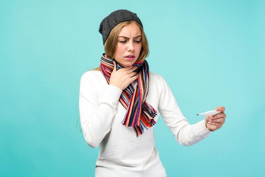 Sad teen girl having flue taking thermometer against blue background. Beautiful lady is sick with a high temperature, isolated close-up. - image