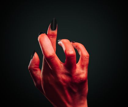 Red demon hand with gesture cross fingers on dark background. Halloween or horror theme