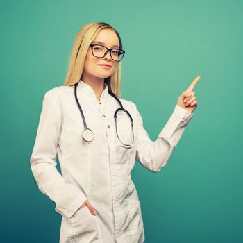 Smiling young medical doctor woman with stethoscope pointing on copyspase. Isolated over blue background. toned
