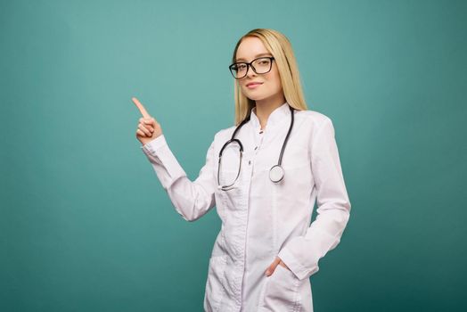 Smiling young medical doctor woman with stethoscope pointing on copyspase. Isolated over blue background.