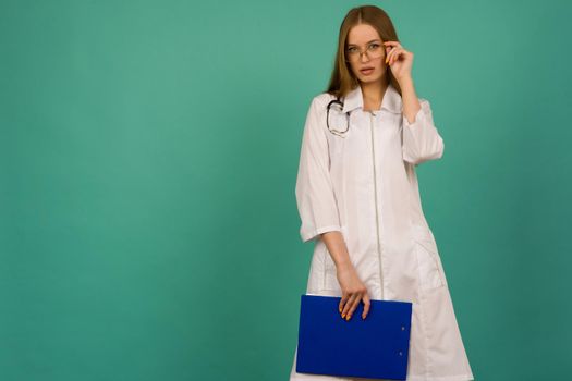 Beautiful young girl nurse or trainee doctor with blue folder and statoscope on a blue background - image