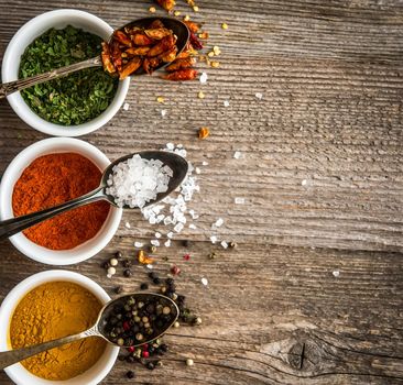 different colorful spicec in bowls and spoons on wooden background