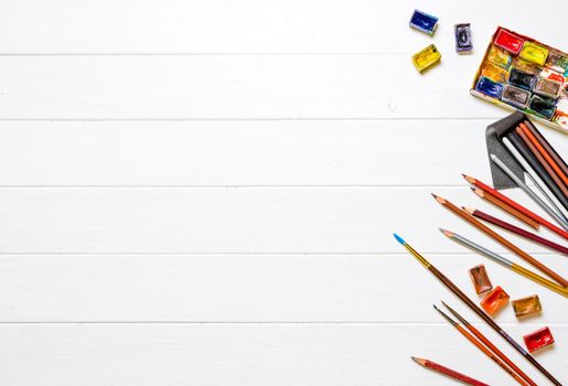 Top view of brushes, gouache and colored pencils on white wooden background. Accessories for drawing. Copyspace, empty space for text