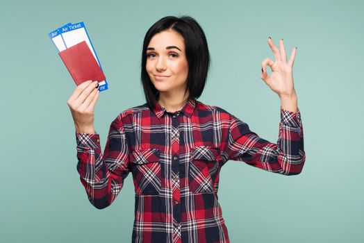 Young shocked excited woman student holding passport boarding pass ticket and showing sing ok isolated on teal background. Education in university college abroad. Air travel flight - Image
